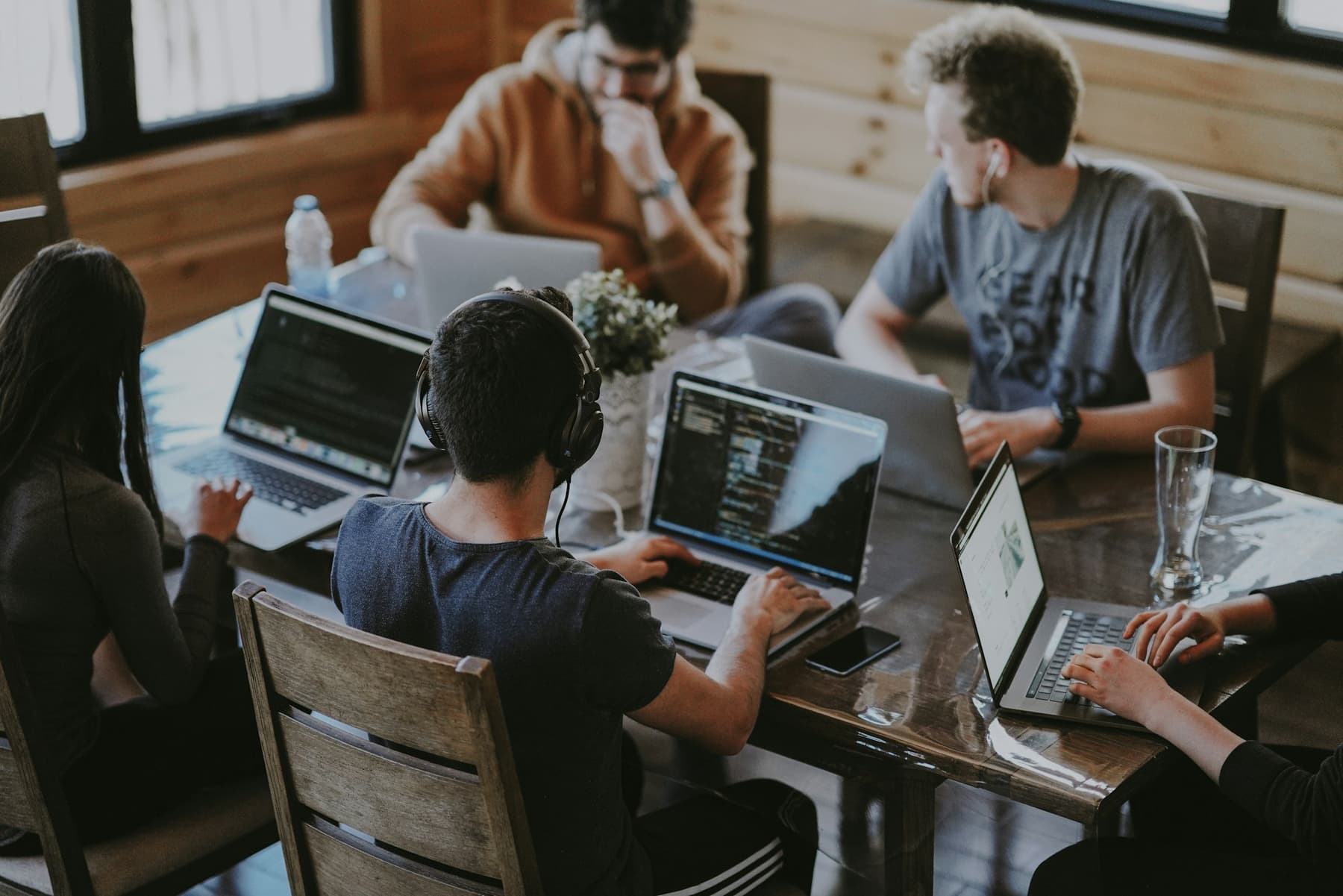 Four people working together around a wooden table with laptops.