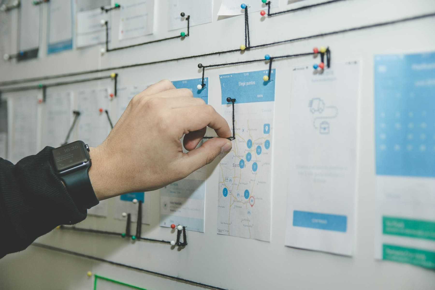 A hand arranging printed screen designs on a planning wall.