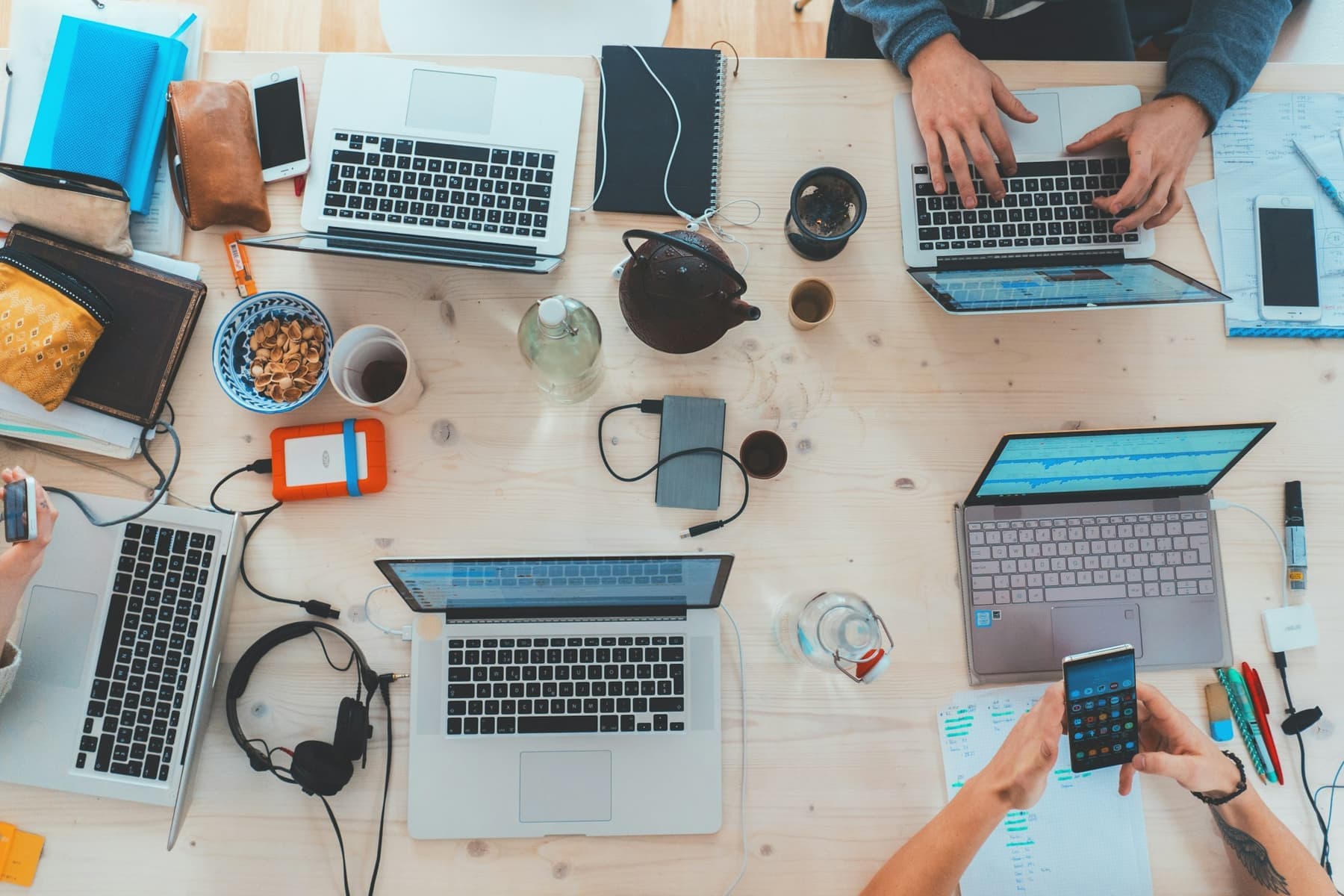 Overhead view of a shared desk with laptops, notebooks and coffee.