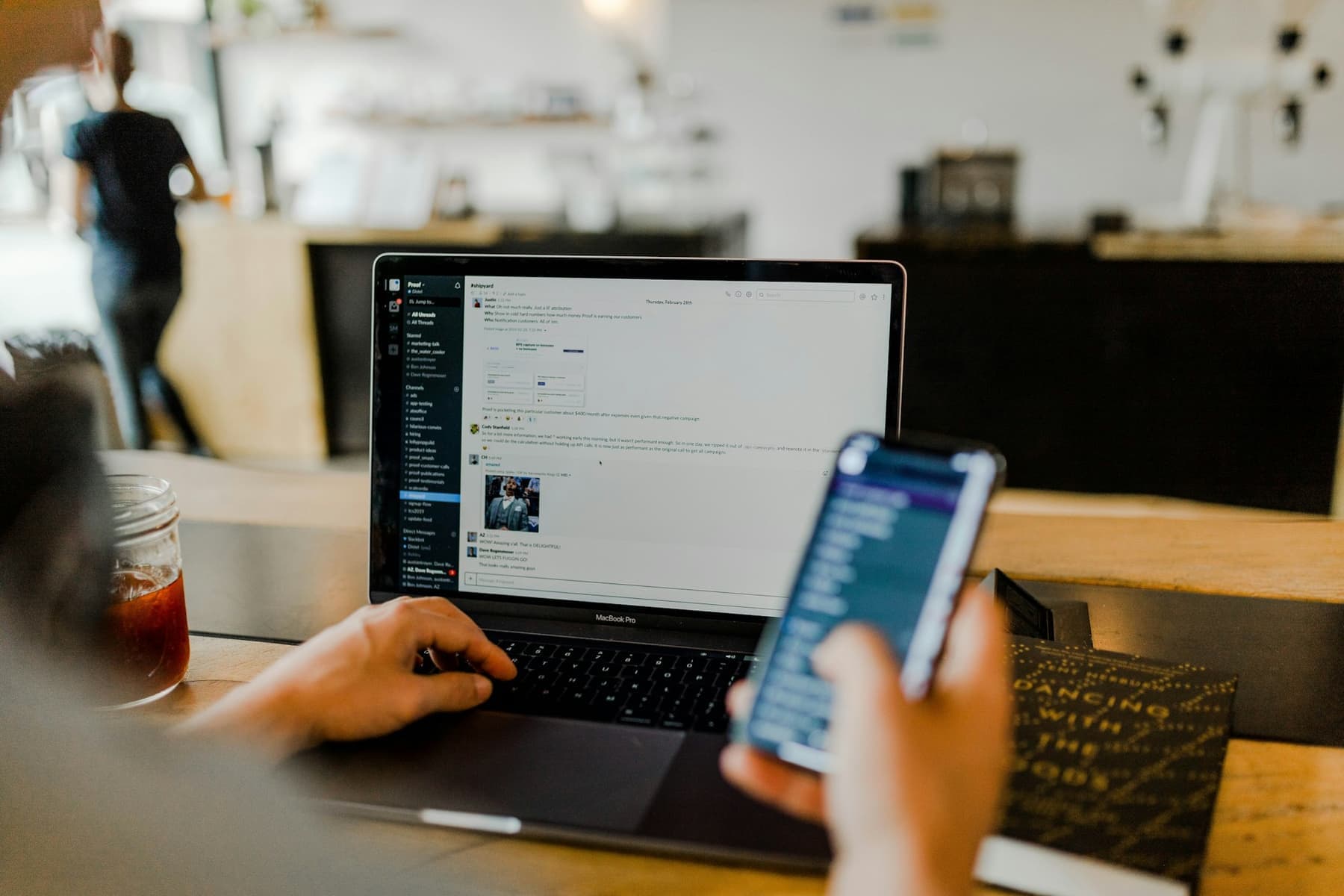 A person using a phone and a laptop at a desk.