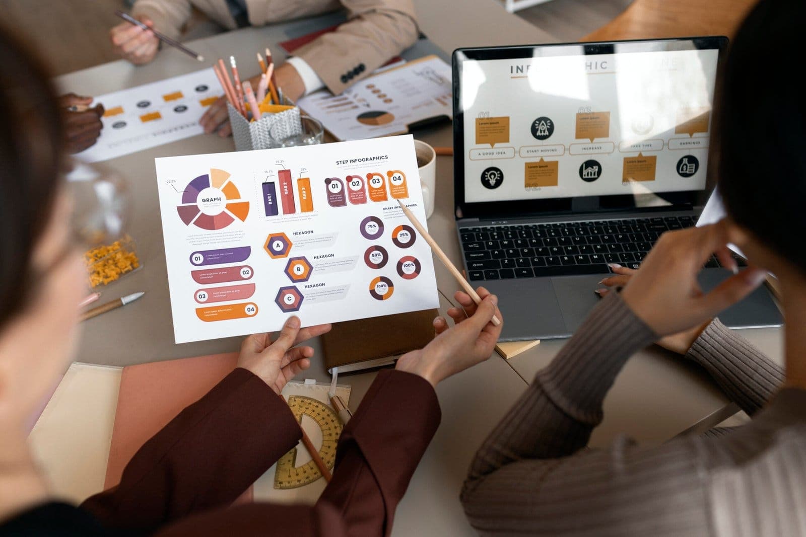 A team reviewing printed infographics and a laptop dashboard around a meeting table.