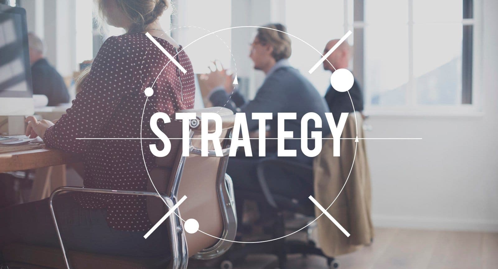 The word “Strategy” in a circular graphic over colleagues meeting in an office.