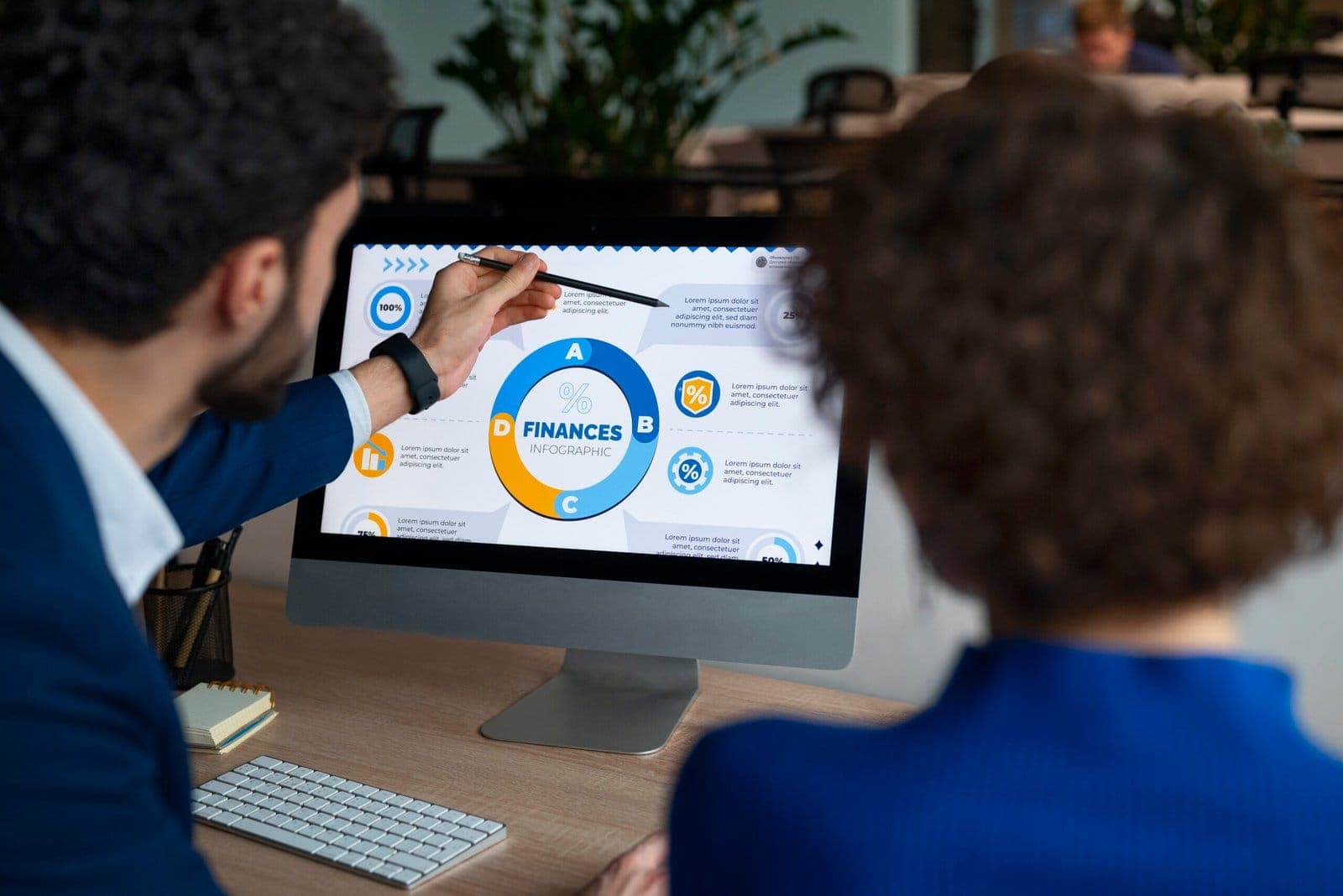 Two colleagues discussing a finance dashboard on a desktop monitor.